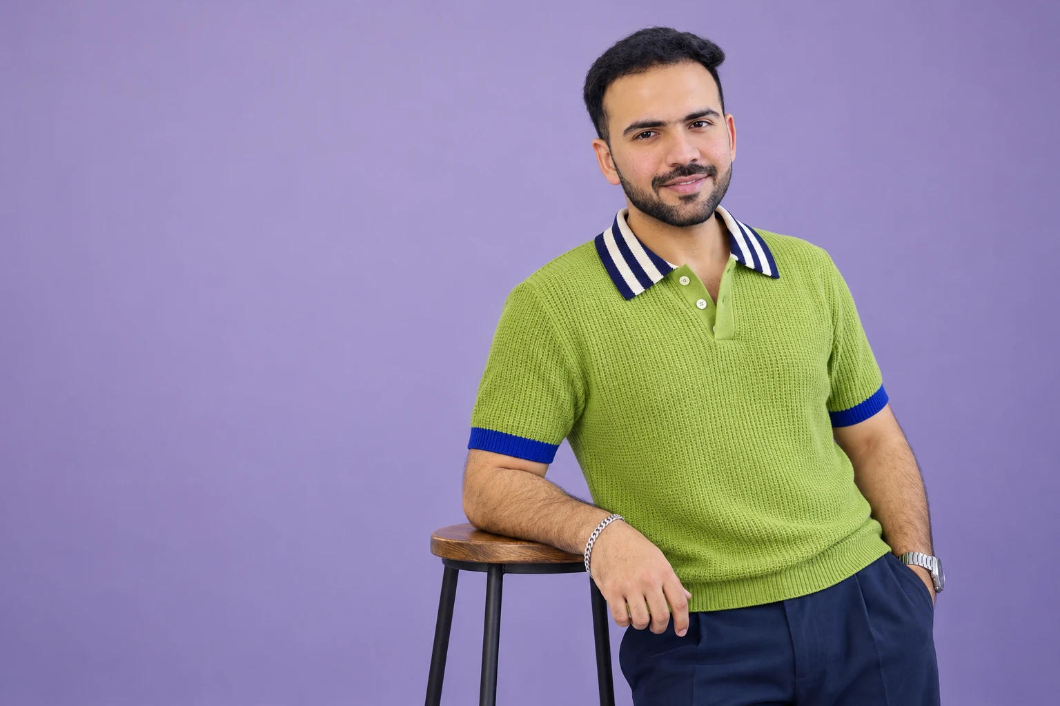 Shivam in a lime textured knit polo, seated casually beside a stool